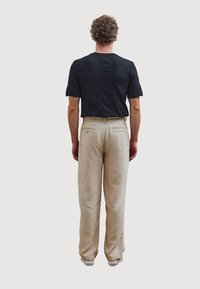 Zwarte, kortekragenshirt met een textuurpatroon; beige, losvallende broek met rechte pijpen en achterzakken; casual schoenen.