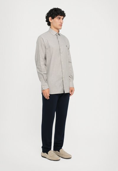 Vaaleanharmaa ruutukuosisella nappipaidalla, jossa on tavallinen kaulus, yhdistettynä tummansinisiin slim-fit-housuihin ja beigen värisiin loafer-kenkiin.