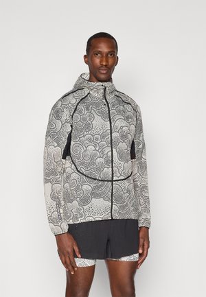 Jacket features a black and white cloud-patterned design, zip closure, and hood. Worn with black shorts that have a textured pattern.