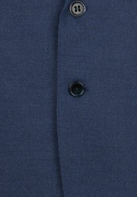 Tmavě modrá látka zblízka, na které jsou dvě černé knoflíky na hladkém texturovaném povrchu, zdůrazňující švy a detaily stehů.