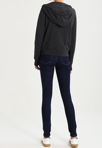 Felpa grigia scura con cappuccio, design corto. Abbinata a jeans skinny blu scuro a vita normale e sneakers bianche con suole beige.