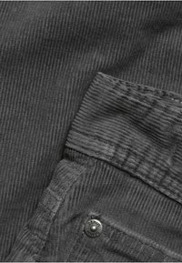 Mörkgrå kordflorts tyg med ribbad textur, med ett tygpatch och en metallknapp med "DENIM" ingraverat.