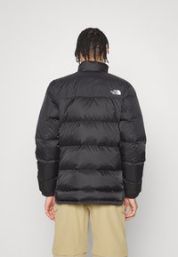 Czarna kurtka puchowa z wysokim kołnierzem i poziomą pikowaną teksturą. Posiada białe logo na górnej części pleców. Lekka i ocieplona konstrukcja.