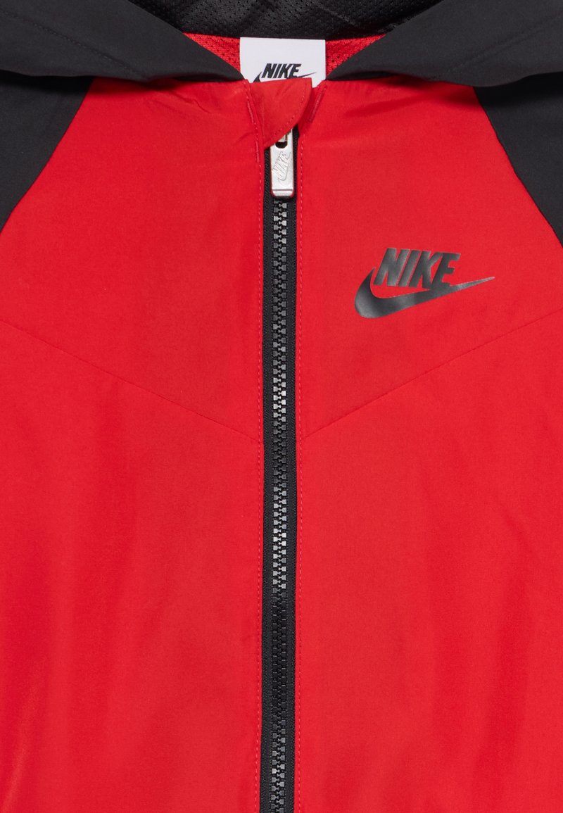 Chaqueta roja con acentos negros, material de nailon, cierre completo, diseño con capucha, con un logo negro de Nike en el pecho.