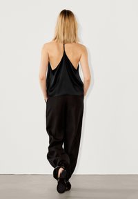 Top nero senza maniche con una vestibilità rilassata e un profondo scollo sulla schiena, abbinato a pantaloni neri a vestibilità rilassata e sandali piatti. Design minimalista.