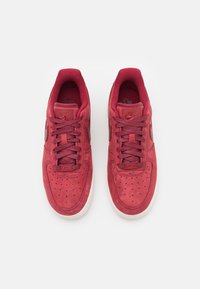 Röda mockaskor med perforerad tåsida, matchande snörning och vit gummisula. Har en logo på tungan och sidan.