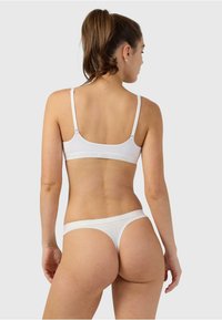 Biely bavlnený bralet a zodpovedajúce tangá s tenkými ramienkami a elastickými pásmi, s hladkou textúrou a minimalistickým dizajnom.
