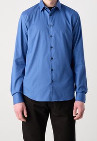 Camicia blu a maniche lunghe con bottoni, caratterizzata da un motivo testurizzato e bottoni neri; il colletto e i polsini sono leggermente più scuri.
