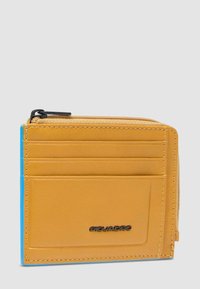 Cartera de cuero color canela con cuatro ranuras para tarjetas, compartimento para monedas con cremallera y logo negro "Piquadro" en la parte delantera sobre fondo gris claro.