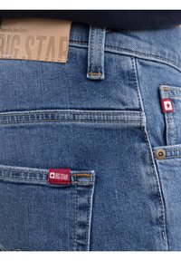 Lähivõte sinistest teksapükstest, tagataskul punased "BIG STAR" kangasmärgid ja vöökohal helepruun nahast brändimärgis.