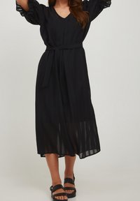 Černé šaty ke kolenům mají nabírané rukávy, výstřih do V, pás na zavázání a texturovanou látku s jemným pruhovaným vzorem.