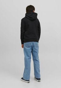 Sudadera con capucha negra y un bolsillo canguro, combinada con jeans azul claro y zapatillas de lona negras. Diseño simple y casual.