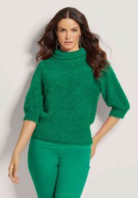 Grüner, flauschiger Rollkragenpullover mit kurzen Ärmeln und geripptem Saum, kombiniert mit passenden grünen, figurbetonten Hosen.