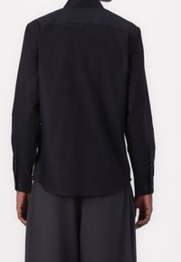 Camicia nera a maniche lunghe con collo a punta, polsini con bottoni e orlo dritto. Tessuto liscio con finitura opaca.