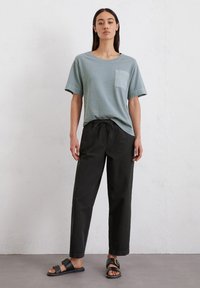 Lichtblauwe T-shirt met korte mouwen en een borstzak, gecombineerd met zwarte broek met trekkoord en zwarte sandalen met een gespsluiting.