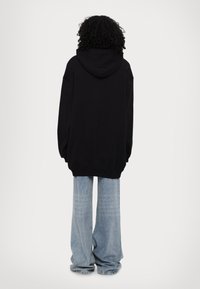 Black oversized hooded sweatshirt with large sleeves, paired with light blue wide-leg jeans. Soft, smooth texture, casual design.
