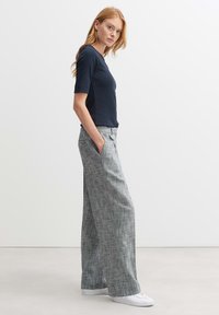 Marineblauwe shirt met korte mouwen, in combinatie met grijs geblokte wijde broek. De broek heeft zijzakken en een losse pasvorm; gestyled met witte sneakers.