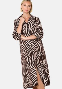 Abito camicia con stampa zebrate in beige e marrone. Presenta maniche lunghe, un colletto e una spacco laterale, realizzato in un morbido tessuto testurizzato.