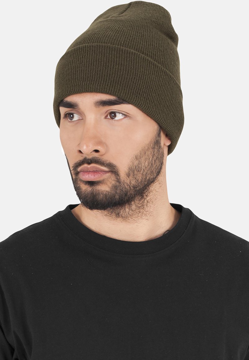 Olive green knit beanie with a ribbed texture, close-fitting design, and a rounded top, worn by a person in a black shirt.
