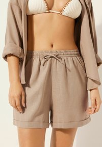 Beiga linshorts med elastisk midja och snörning, med sidofickor och rullade fållar. Matchas med en texturerad bikiniöverdel.
