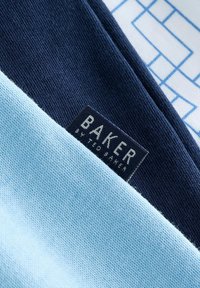 Close-up van dubbelgevouwen stof in lichtblauw en marineblauw met een zwart etiket waarop staat "BAKER BY TED BAKER" op het marineblauwe gedeelte.