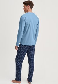 Haut à manches longues bleu clair associé à un pantalon de pyjama navy à motifs avec de petites formes blanches, fabriqué en tissu doux et respirant.
