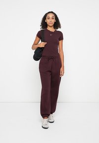 Bordeaux sportoutfit met een aansluitend t-shirt en losse joggers, gemaakt van zachte stof met een elastische tailleband. Gecombineerd met witte sneakers.