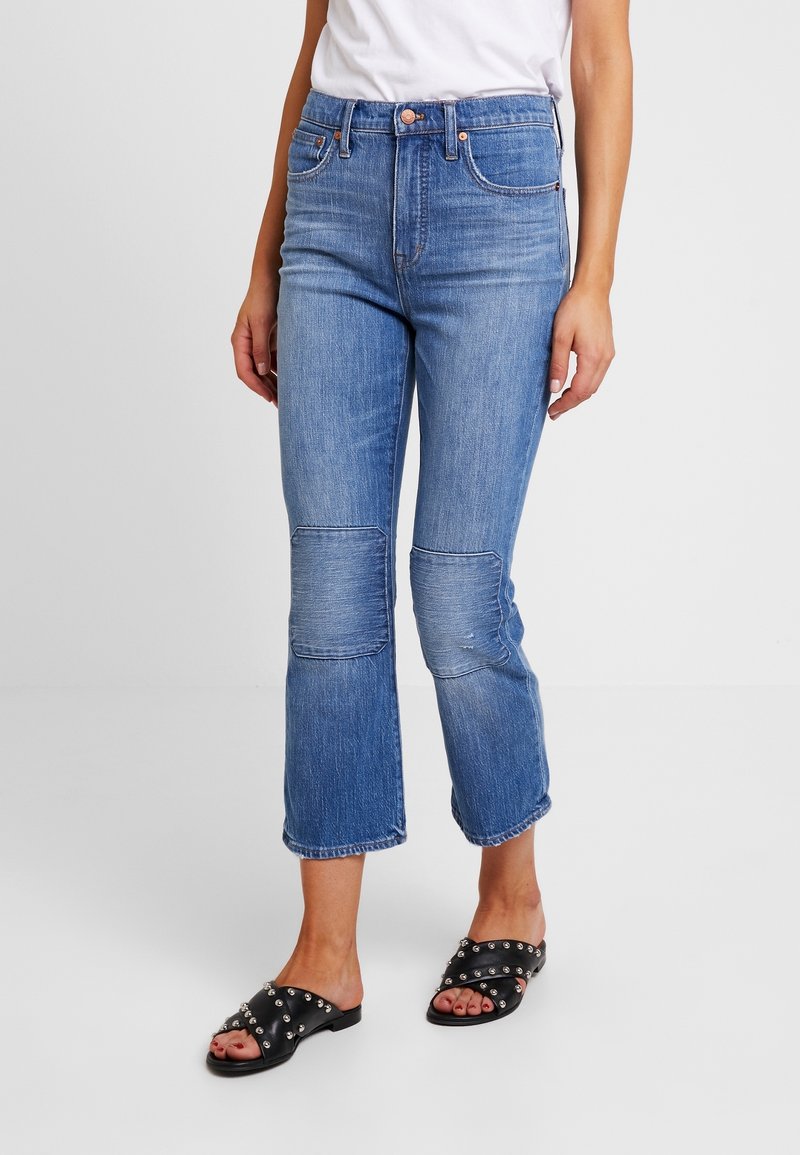 Ljust blå denimjeans med hög midja, lätt utsvängda ben och lappar på knäna. Kombineras med svarta sandaler med nitar.