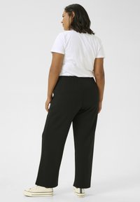 Pantalon large noir en tissu doux, doté d'une taille élastique. Assorti à un t-shirt blanc et des baskets beiges.