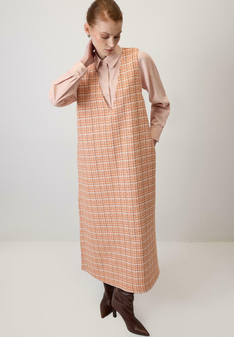 Orange and cream plaid long dress with a V-neck, layered over a light pink button-up shirt. Brown pointed toe boots complete the look.