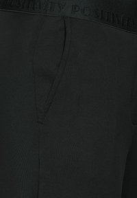 Černé tepláky s měkkou texturou, s širokým pasem s embosovaným nápisem „POZITIVITA“ a bočními kapsami.