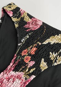 Blommig baddräktstopp med svart botten, som har smockad tyg i nyanser av rosa, röd och grön blommönster; slät struktur.