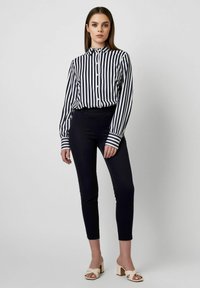 Button-down shirt with navy and white vertical stripes, paired with dark trousers and light-colored heeled sandals. Smooth fabric texture.