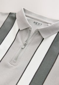 Harmaa ja valkoraidallinen poolopaita vetoketjulla edessä, jossa on pehmeä pinta ja kauluksellinen pääntie. Brändilaatta näkyvissä.