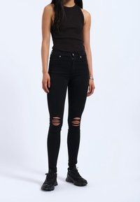 Svarta slitna jeans med slim fit och hög midja, gjorda av denim. Kombinerade med en åtsittande brun linne och svarta sneakers.