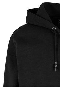 Sweatshirt à capuche noire avec une texture lisse, un cordon de serrage réglable et une coupe décontractée. Aucun motif ni logo visible.
