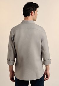 Camisa gris de manga larga con cuello abotonado, puños enrollados y dobladillo recto. Hecha de una tela texturizada, presenta un diseño simple.