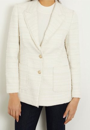 Tweed blazer in off-white met een gestructureerd patroon, met klepjes, twee voorzakken en twee knopen. Gestiileerd met donkere spijkerbroeken.