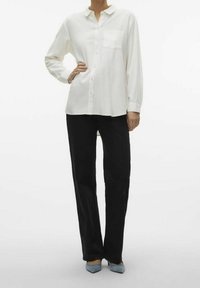 Valkoinen pitkähihainen kauluksellinen nappipaita etutaskulla, yhdistettynä mustiin suora lahkeisiin housuihin ja vaaleansinisiin teräväkärkisiin korkokenkiin.