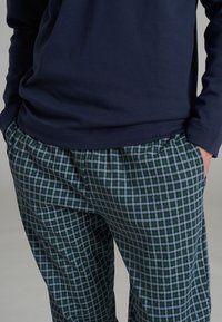 Maglietta a maniche lunghe di colore navy abbinata a pantaloni pigiama a quadri verdi e blu. Tessuto in cotone, vestibilità comoda, vita elastica e tasche laterali.