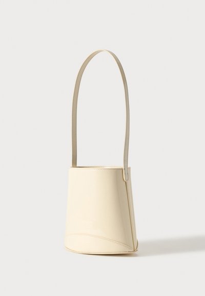 Sac seau en cuir couleur crème avec une longue bandoulière fine, présenté sur un fond clair uni.
