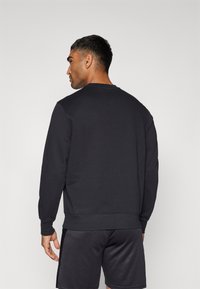 Sort sweatshirt med lange ærmer og rund hals, med et ensfarvet design og en behagelig pasform. Bæres med mørke shorts.