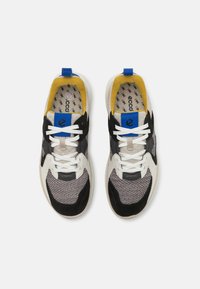Αθλητικά παπούτσια με πλέγμα σε γκρι, μαύρο και λευκό, με μπλε και κίτρινες λεπτομέρειες, λευκά κορδόνια και καουτσούκ σόλα.