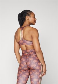 Sports-bh og leggings i en lilla-brun nyanse med et palme tre mønster; har racerback design og subtile striper.