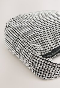 Silver rhinestone-embellished handbag with a rounded shape, black accents, zipper closure, and a glittering texture covering the exterior.