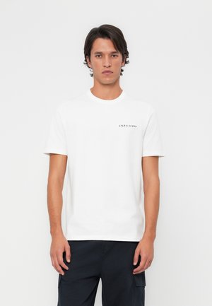 White cotton t-shirt with short sleeves and a round neckline, featuring a subtle black logo on the left side, worn with dark pants.