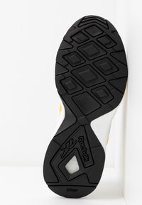 Černá gumová podrážka tenisky Reebok s geometrickým vzorem běhounu a viditelným bílým odpružením skrze výřez.