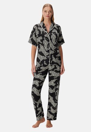 Kvinde iført sort- og hvid tigerprint kortærmet knap-op top og matchende lange pyjamasbukser, stående barfodet.