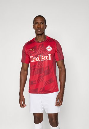 Rotes Fußballtrikot mit kurzen Ärmeln, grafischem Muster, Rundhalsausschnitt und Logo-Details. Kombiniert mit weißen Shorts, die ein sportliches Design präsentieren.