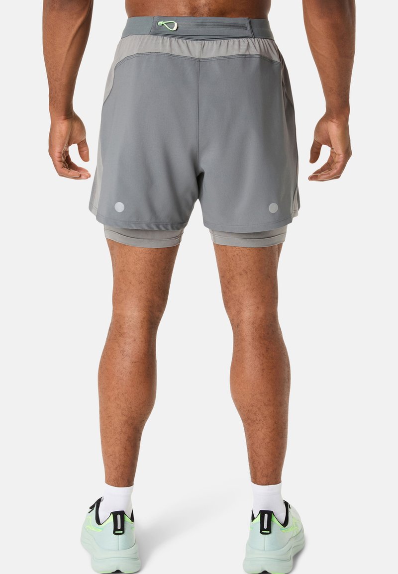 Shorts de sport gris au design léger, dotés d'une taille avec cordon de serrage et d'accents réfléchissants. Portés par-dessus un short intérieur assorti.